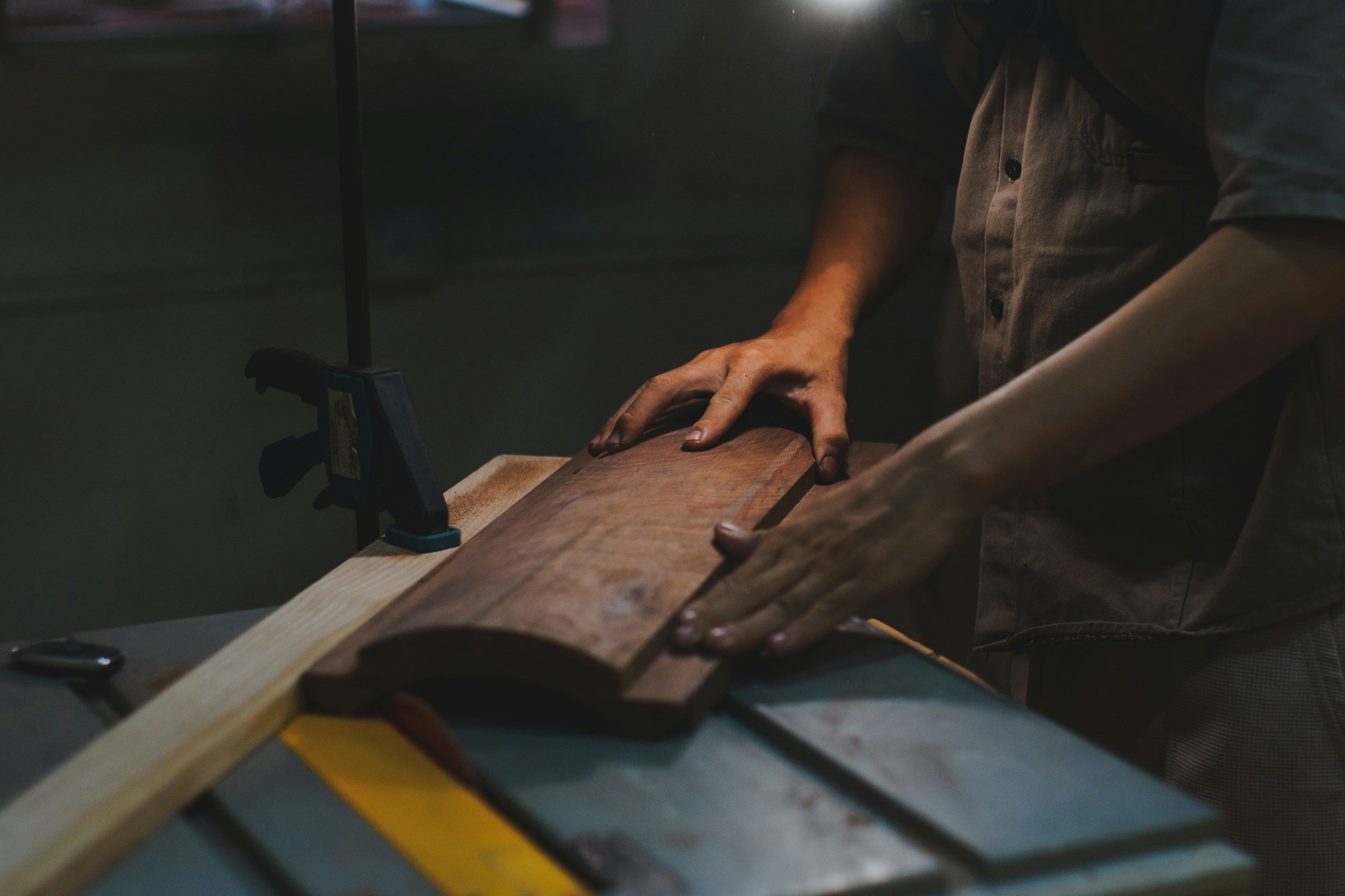 A carpenter’s hands working a dark timber piece on a workshop bench.