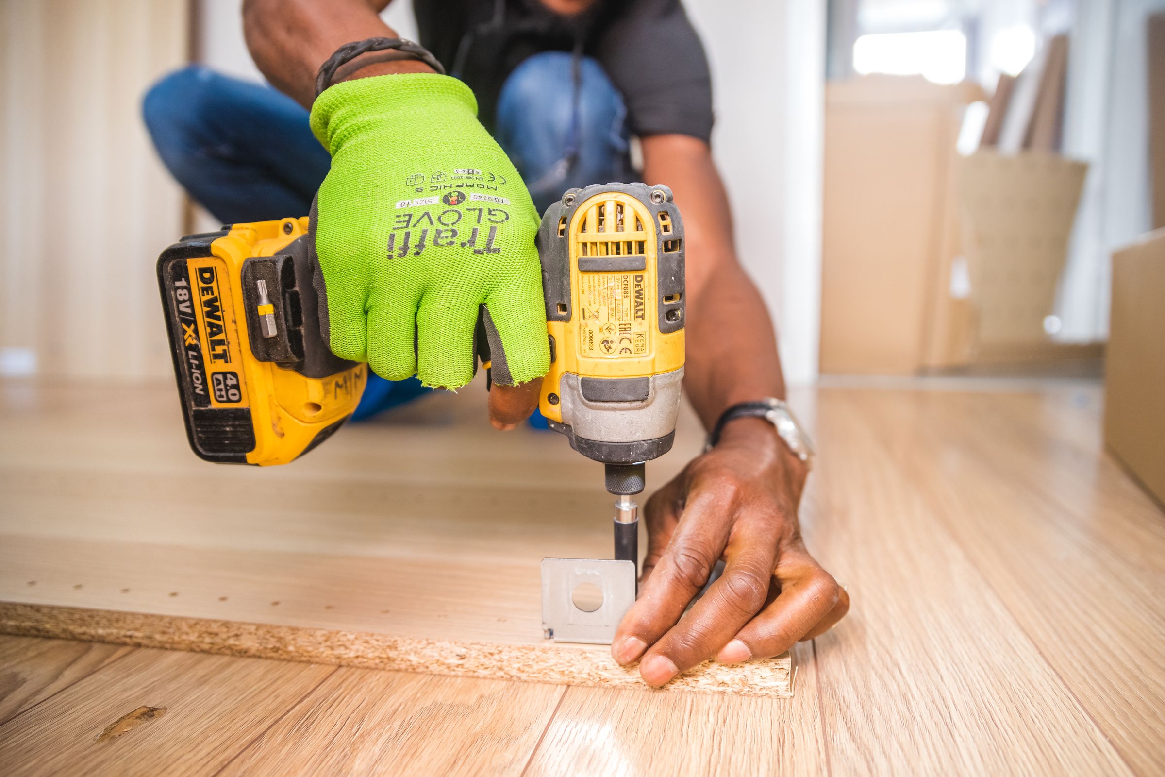 Hands using an impact driver to fix a metal bracket to a timber board.