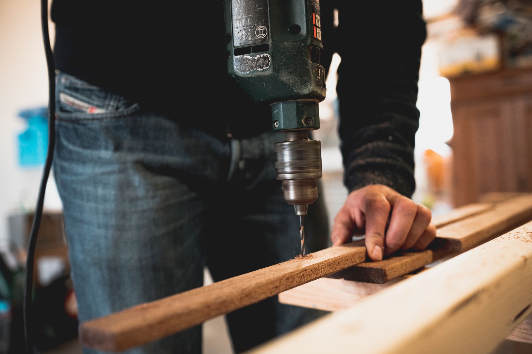 A drill bit entering a timber plank on a workbench.