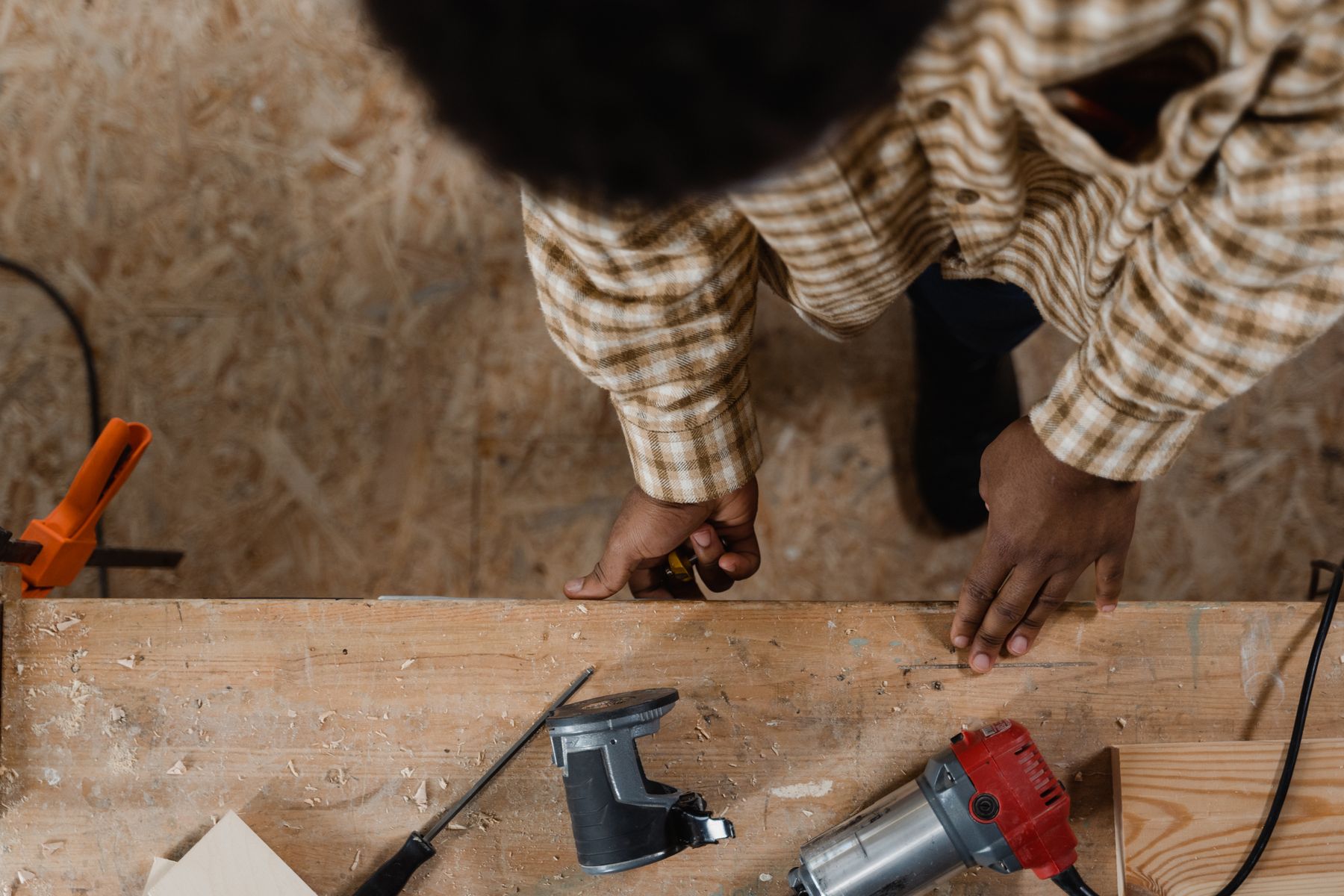 Overhead view of a carpenter at a timber workbench with routers, clamps, and offcuts.