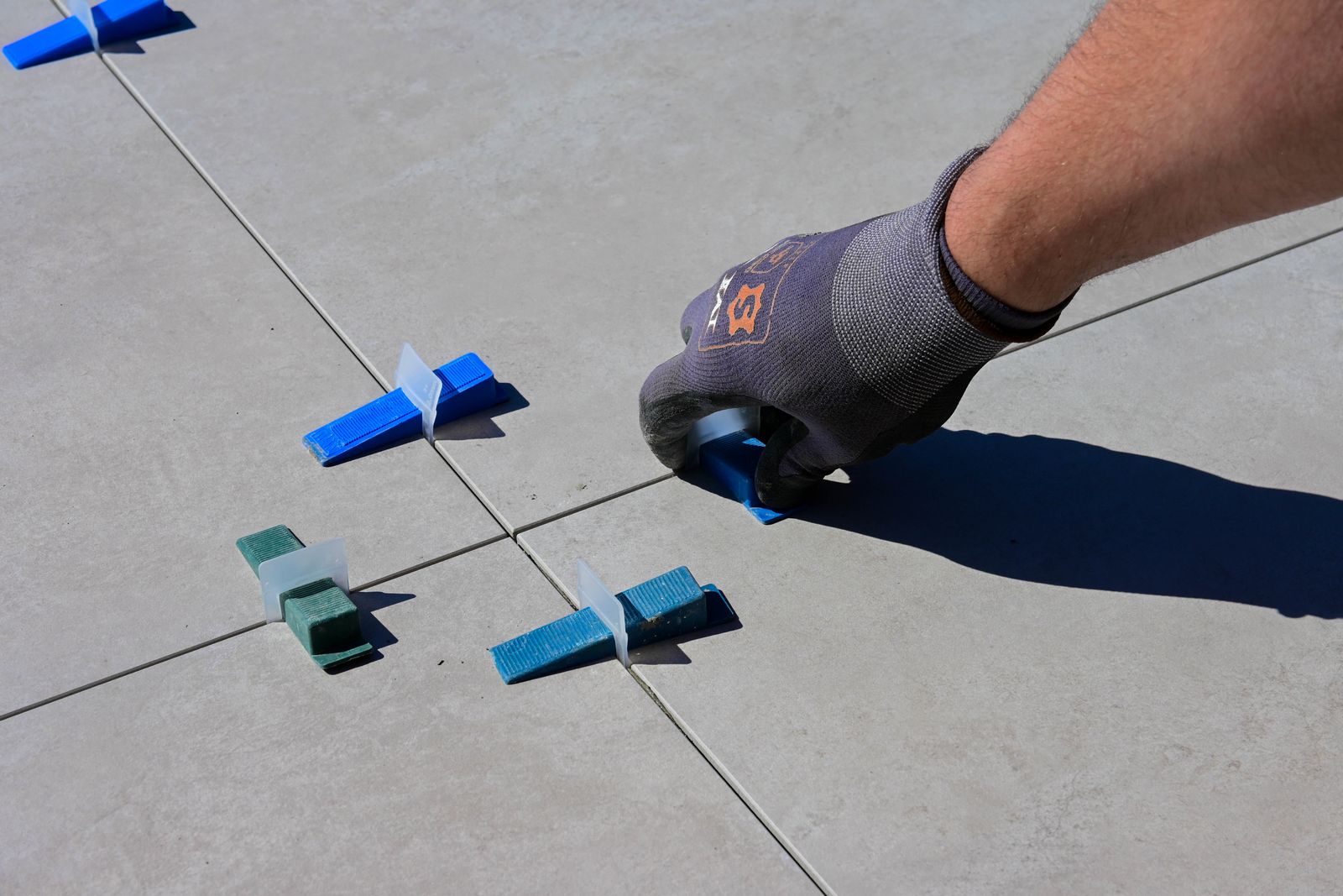 A gloved hand setting tile spacers on a light floor.